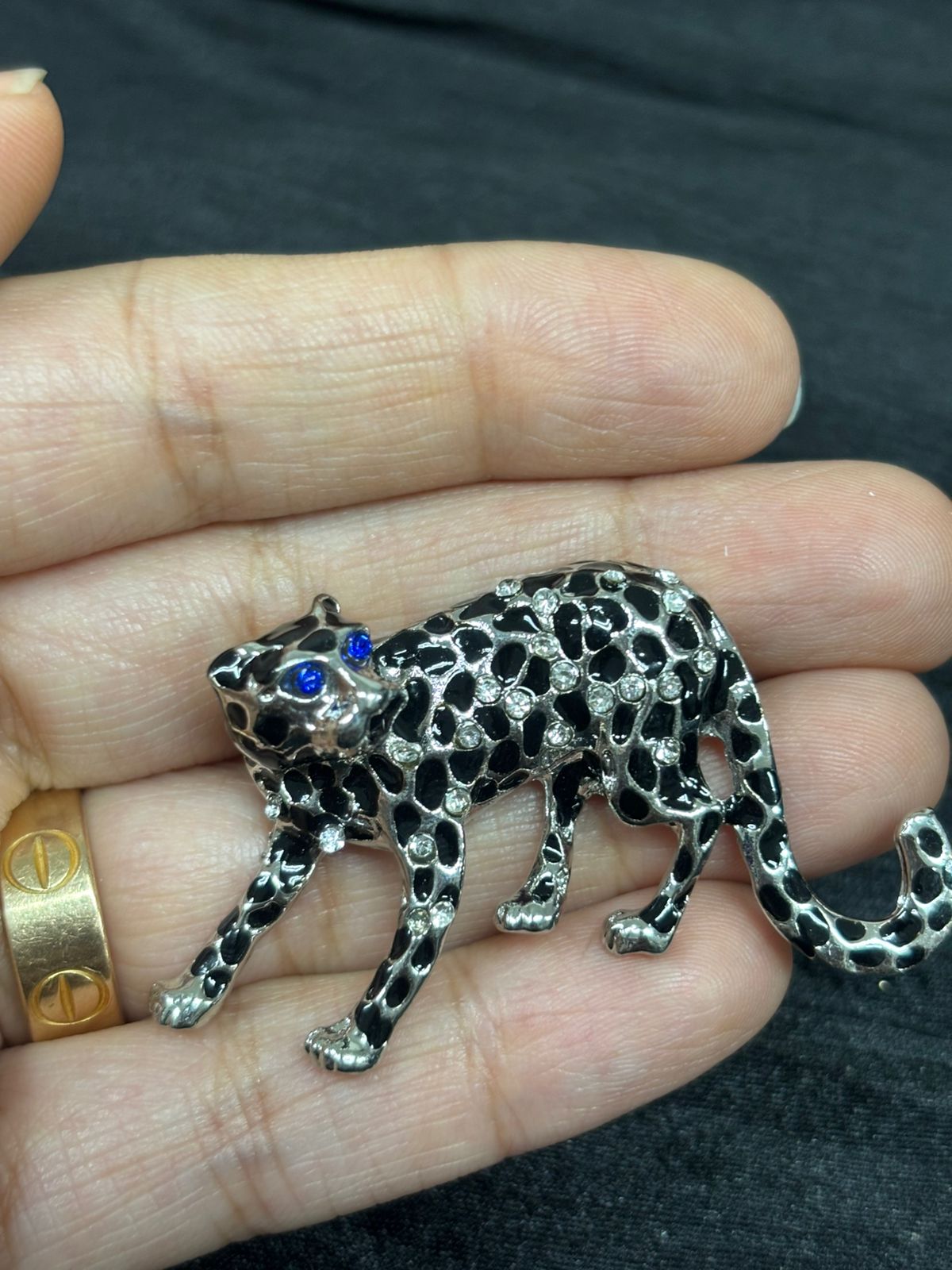 Silver leopard pendant with blue gemstone held in a hand against a dark background