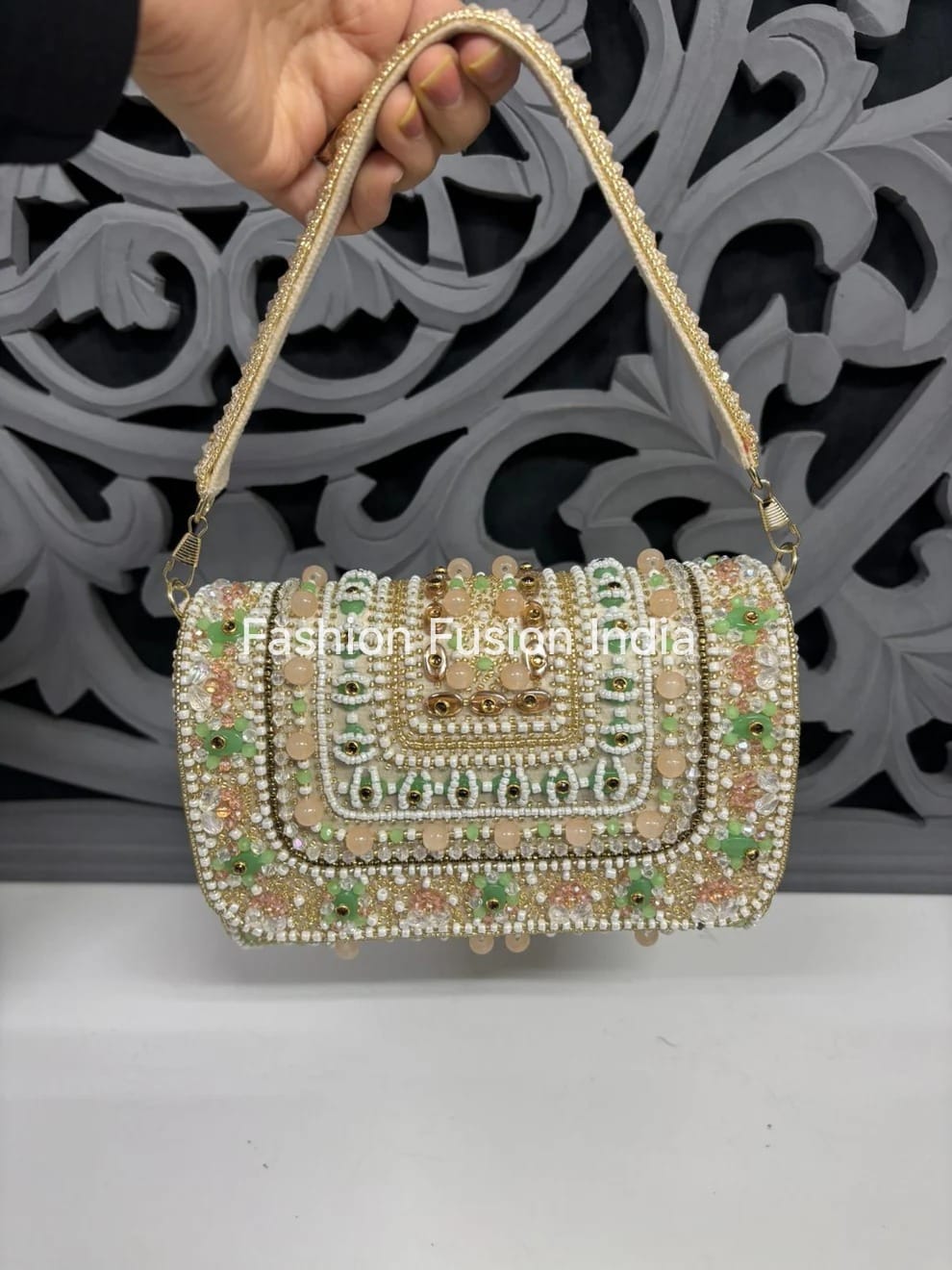 Decorative handbag with intricate design held by a hand against a decorative wall.