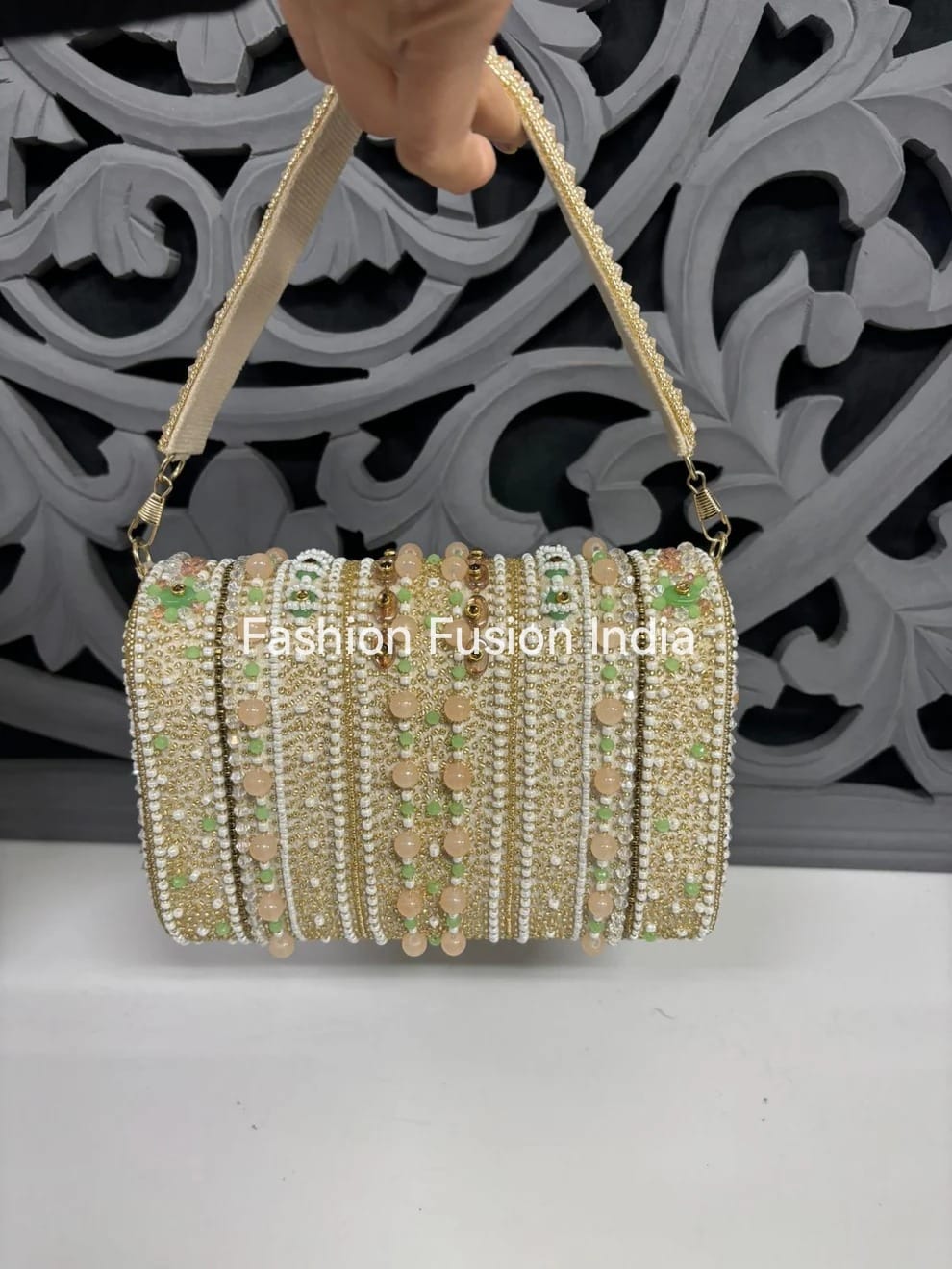 Decorative handbag with beaded details held by a hand against an ornate background.