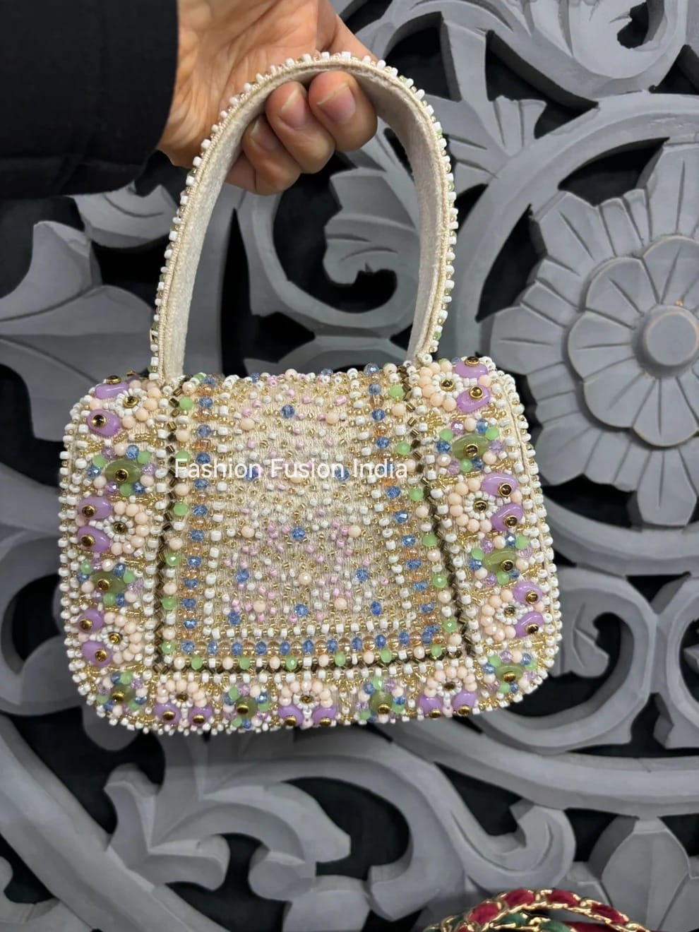Decorative handbag with beaded details held by a hand against an ornate background.