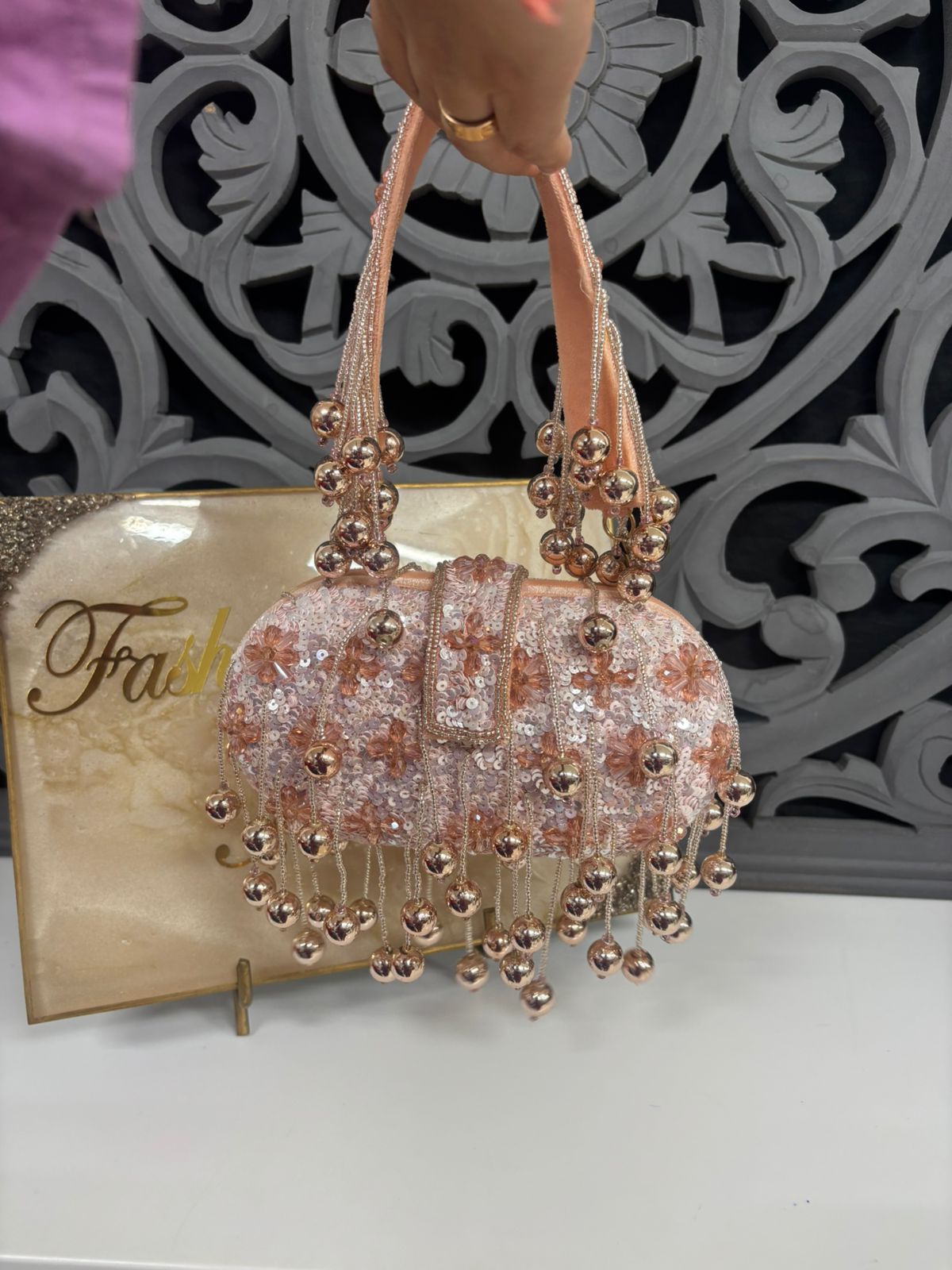 Decorative handbag with beaded details on a stand against an ornate wall.
