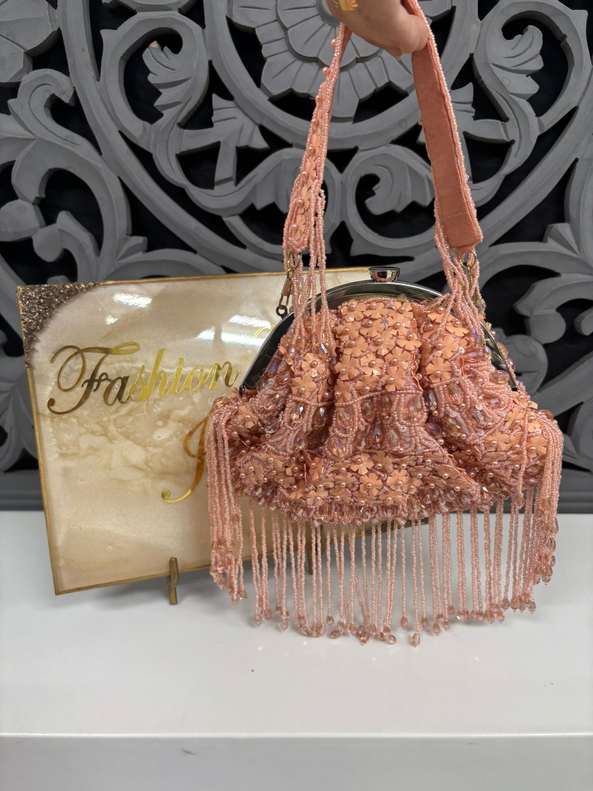 Rose gold beaded handbag with fringe on a white surface with a decorative background.