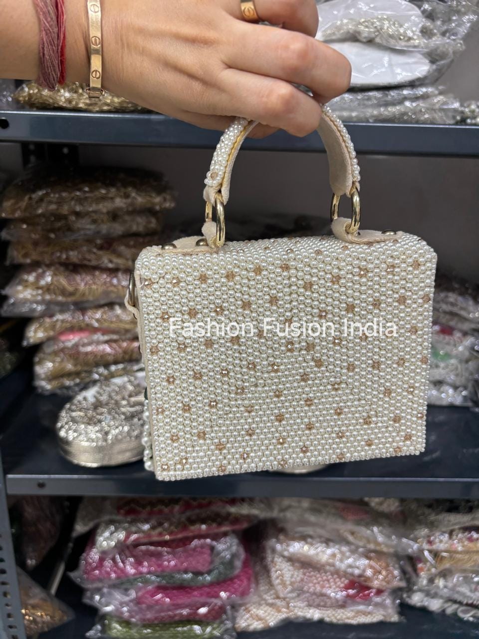 Handheld pearl-handled handbag with 'Fashion Fusion India' branding against a blurred background.