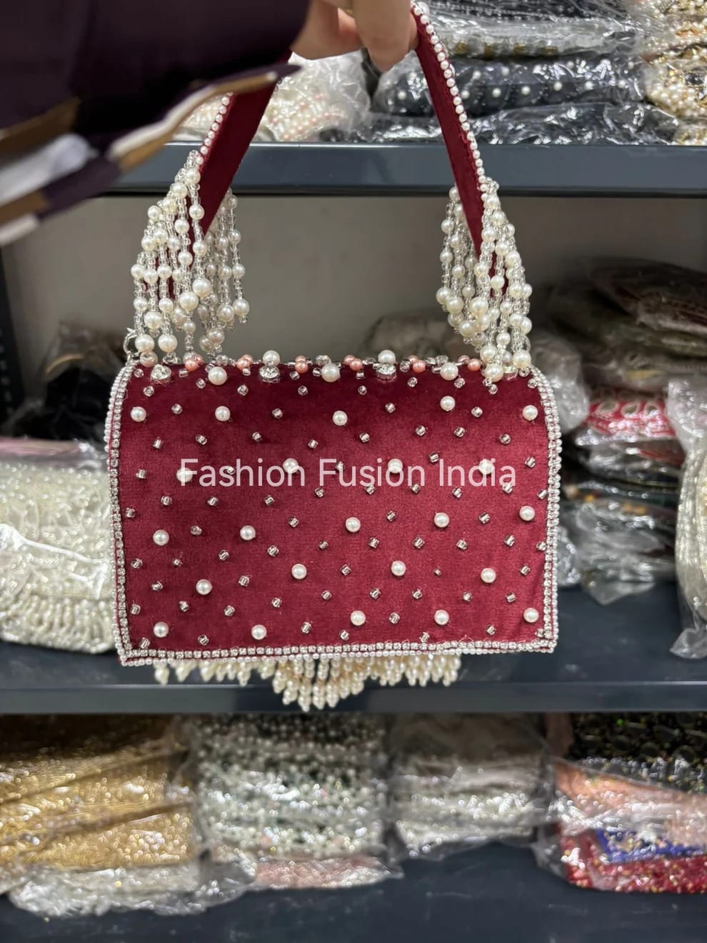 Red handbag with pearl embellishments held above a display of similar bags.