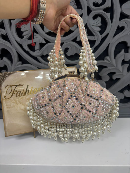 Decorative handbag with pearl details held by a hand, with 'Fashion' book in the background.