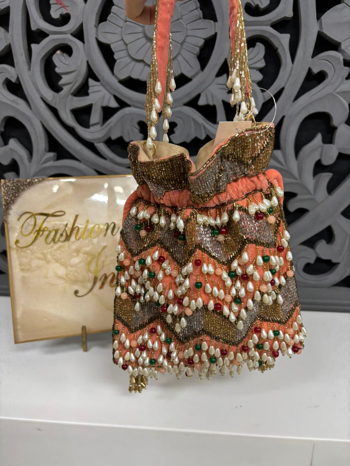 Decorative handbag with intricate patterns and beads on a white surface with 'Fashion India' sign.