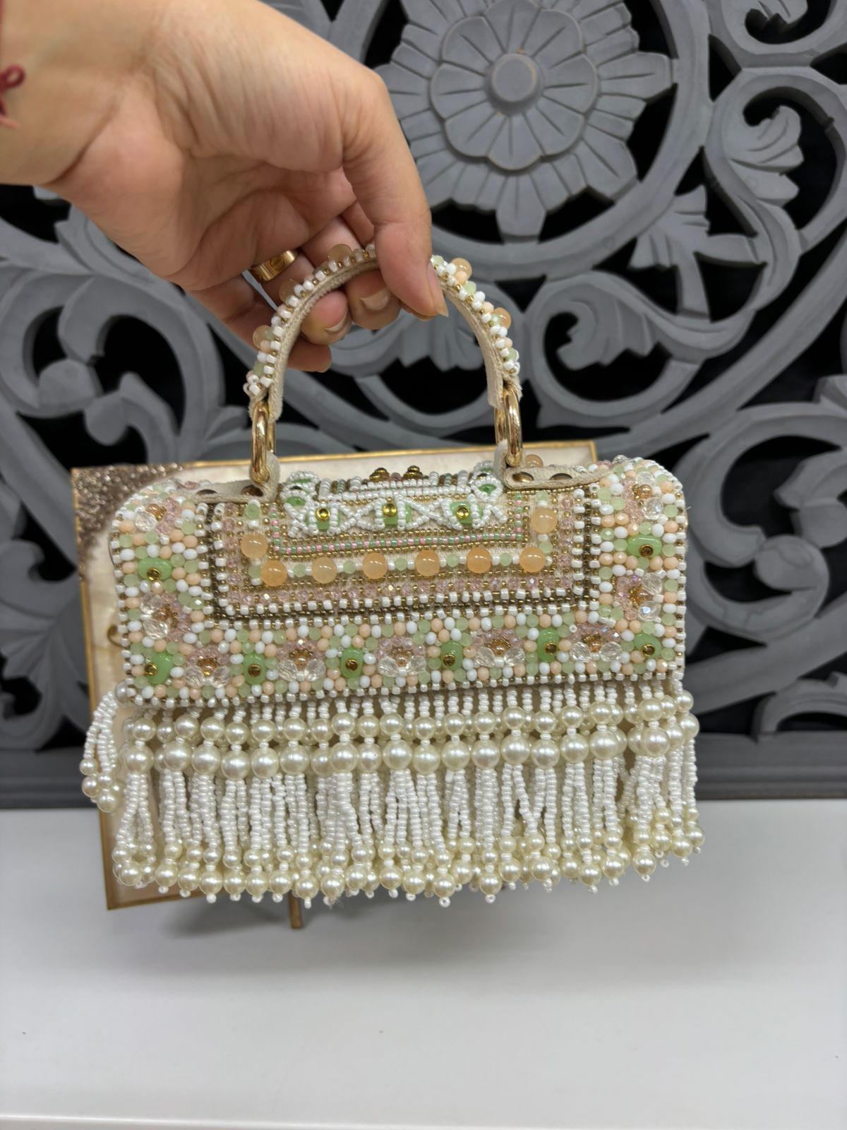 Handbag with beaded design held by a hand against an ornate decorative background