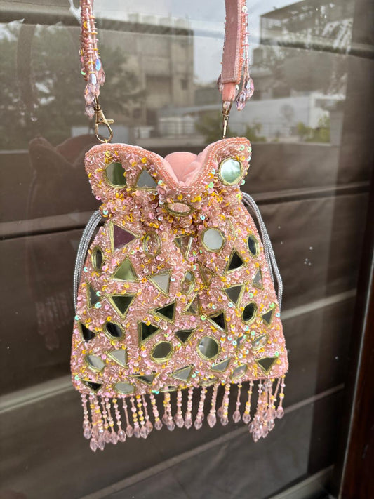 Decorative handbag with beaded design and pink strap on a reflective surface