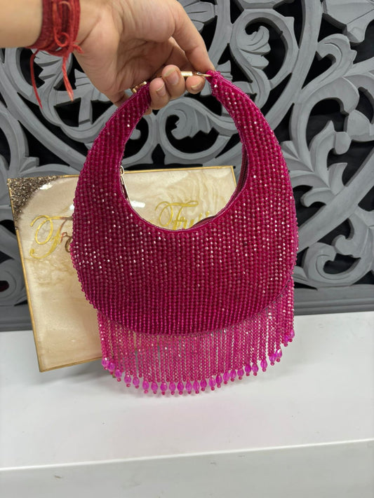 Pink beaded handbag held by a hand with a red bracelet against a decorative background.
