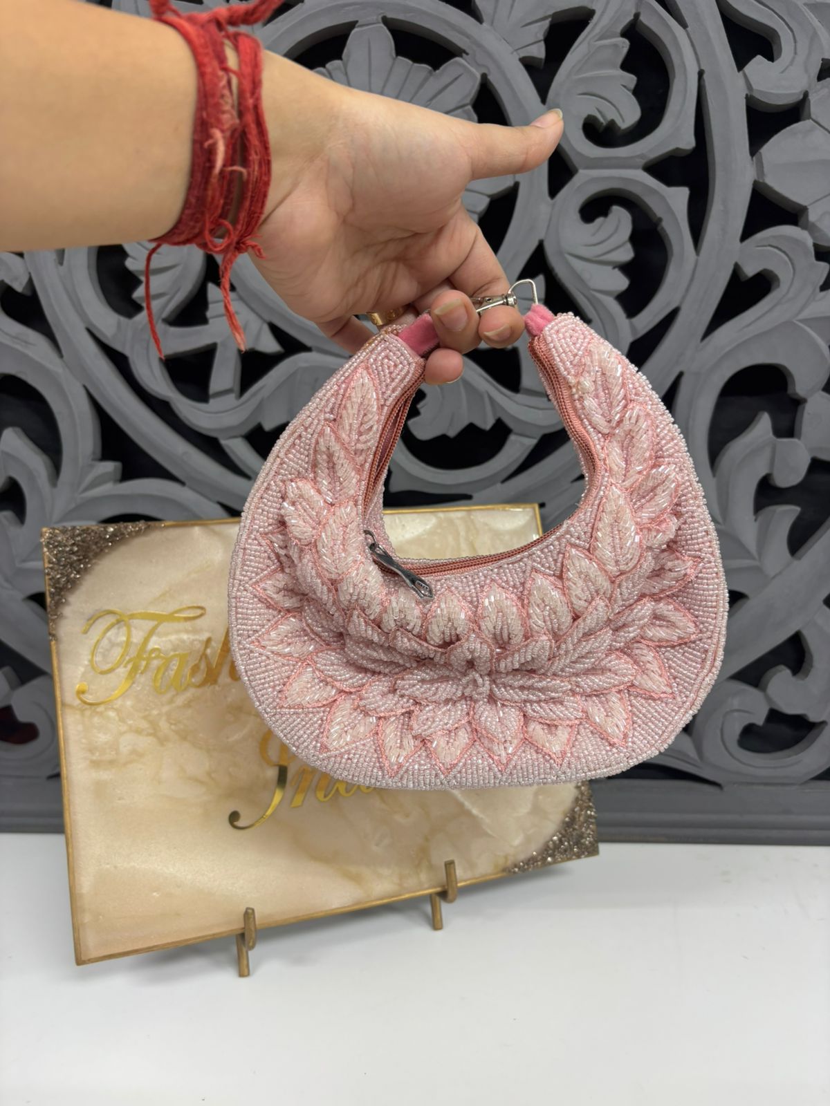 Pink beaded handbag held by a hand with a decorative background
