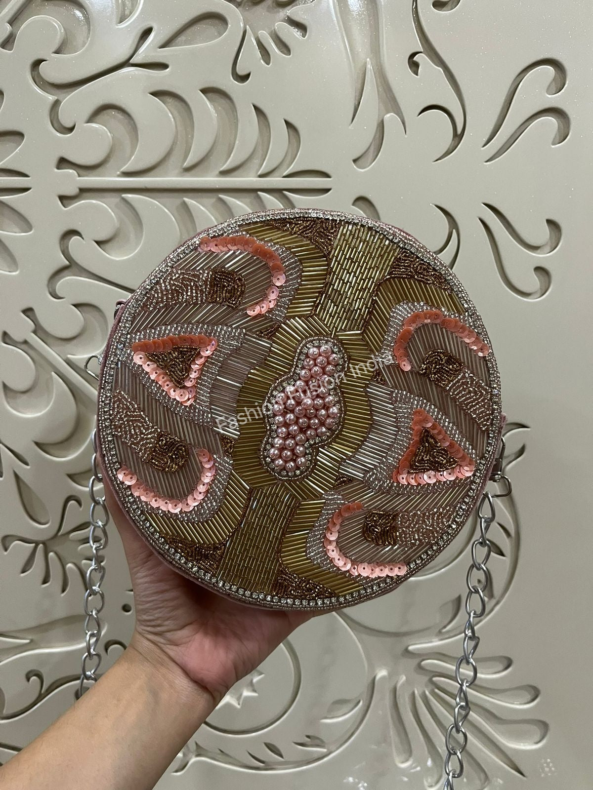 Round embroidered bag held by a hand against a decorative white background