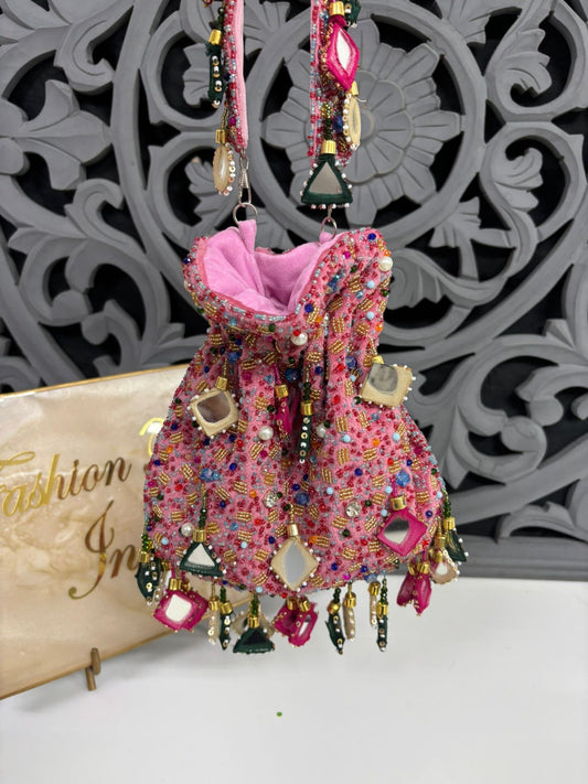 Decorative pink bag with embellishments on a white surface with a decorative gray background.
