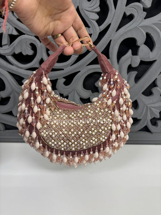 Handbag with bead and pearl detailing held by a hand against an ornate gray background