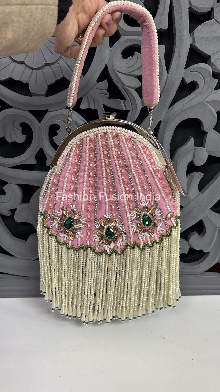 Decorative handbag with pink top handle and green embellishments on a white surface.