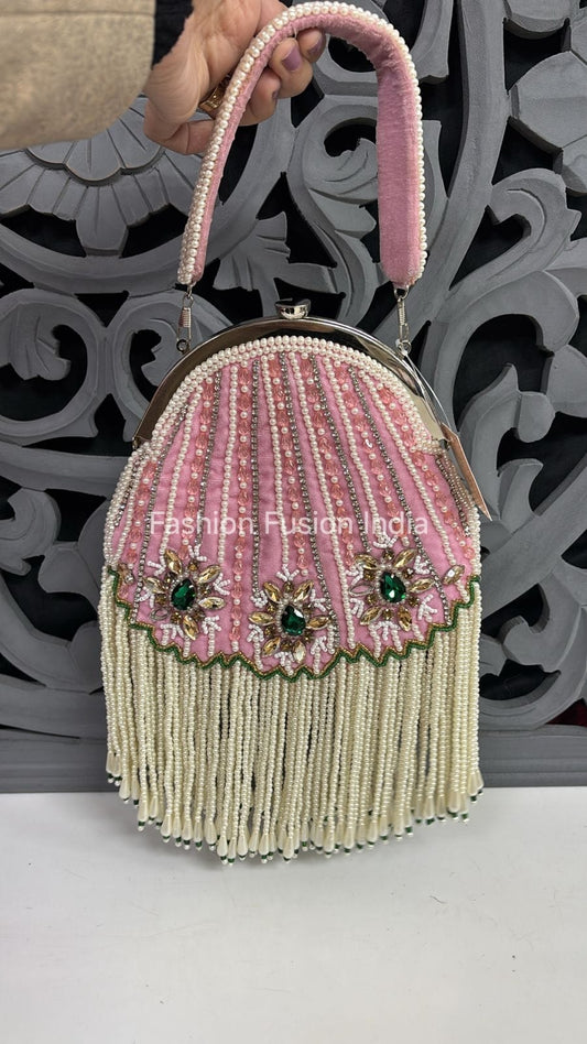 Decorative handbag with pink top handle and green embellishments on a white surface.