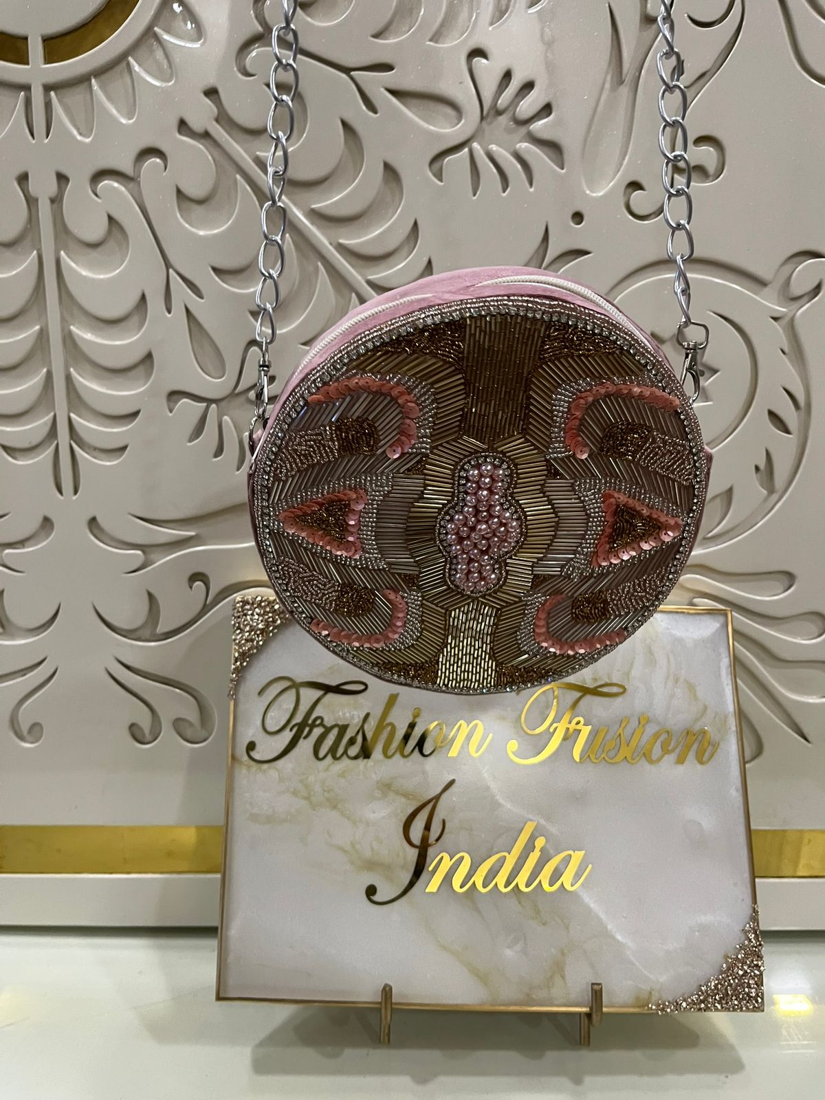 Decorative handbag with intricate designs on a stand with 'Fashion Fusion India' branding.