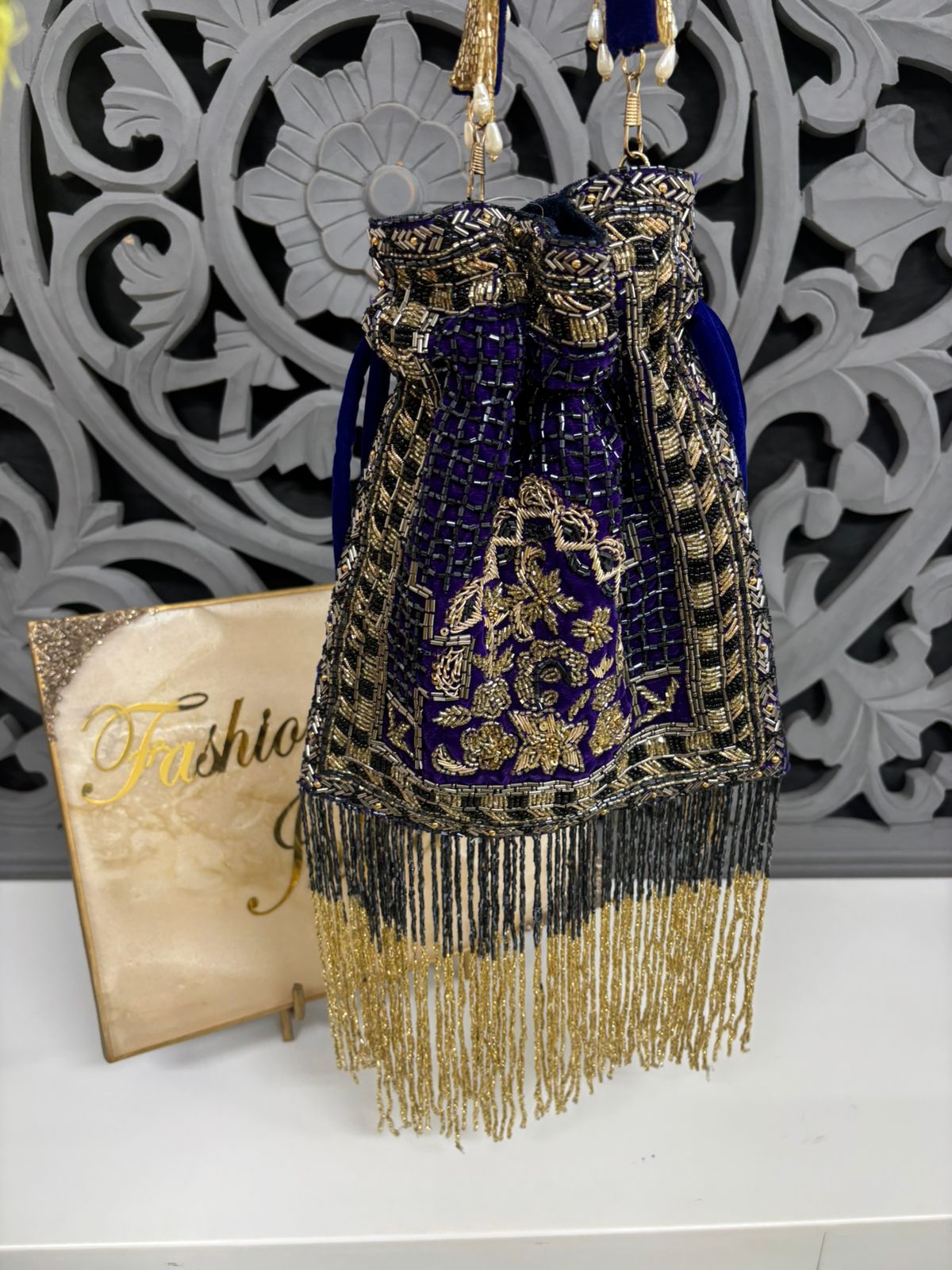Decorative handbag with gold and blue details on a white surface with a decorative wall in the background.