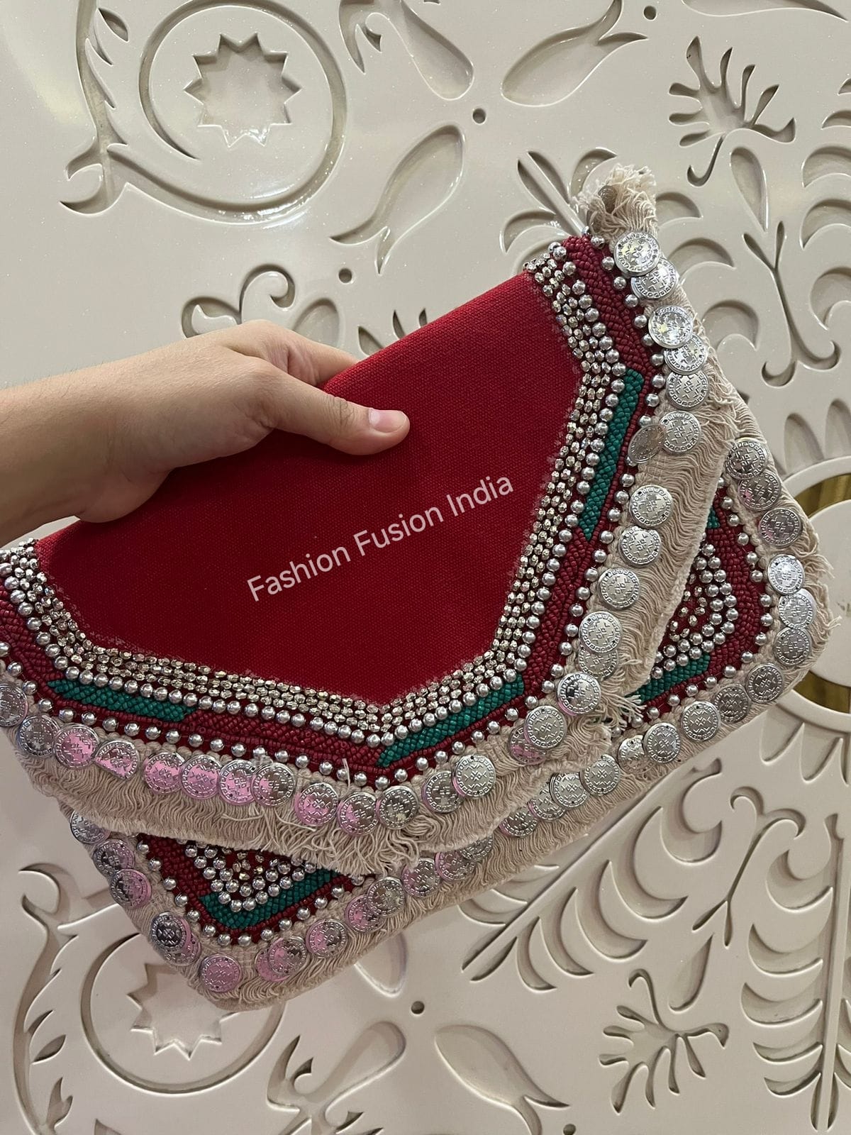 Decorative clutch with intricate designs held by a hand against an ornate white background.