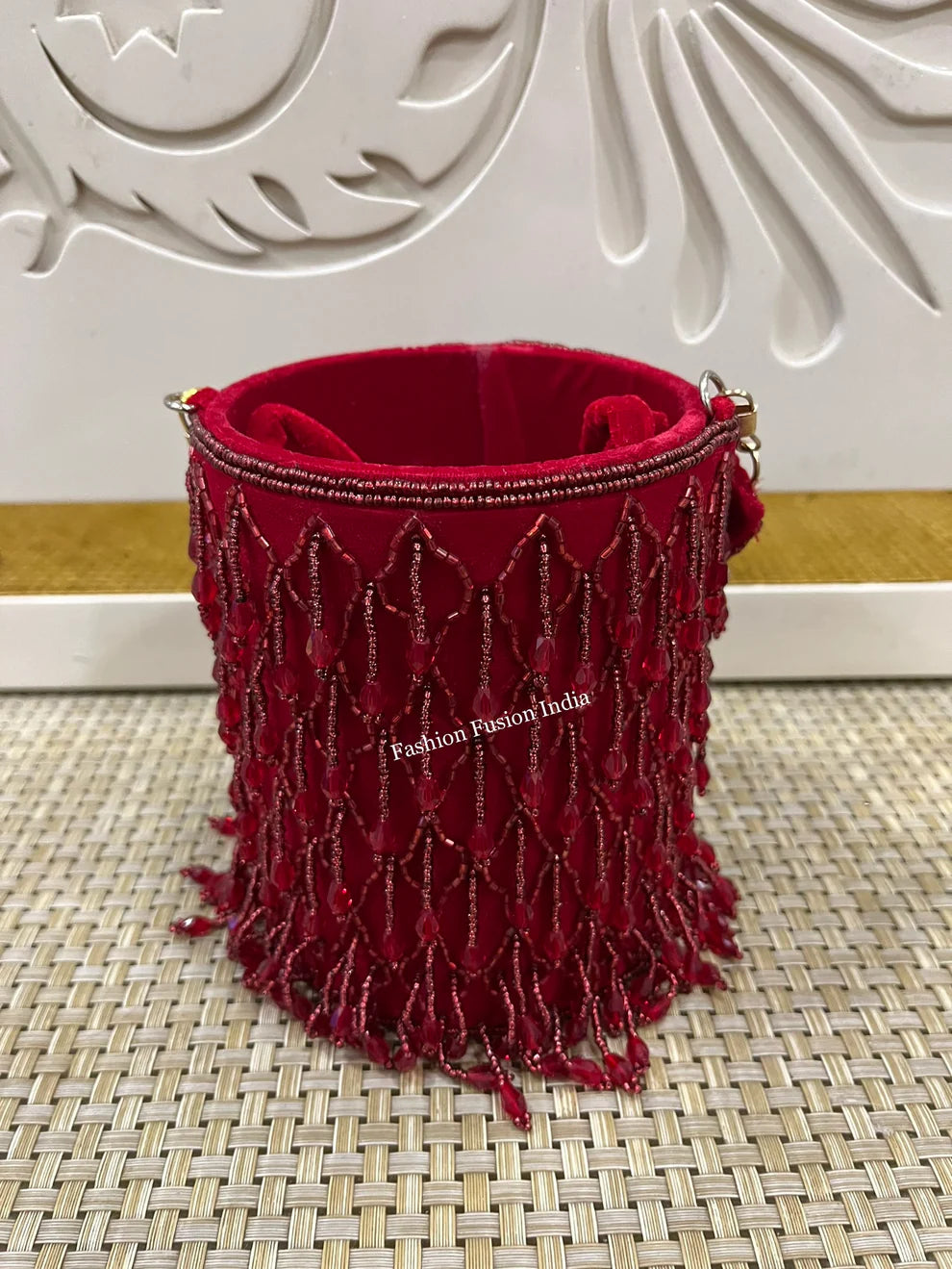 Red beaded pouch on a textured surface with a decorative white wall in the background