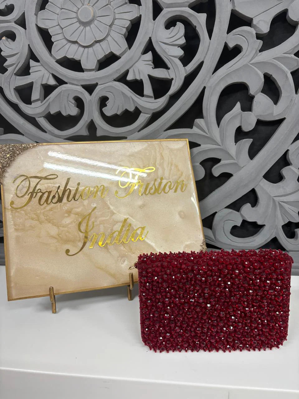 Red beaded clutch bag next to a 'Fashion Friston India' sign on a decorative background