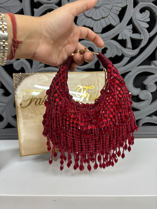 Red beaded handbag held by a hand with a decorative background