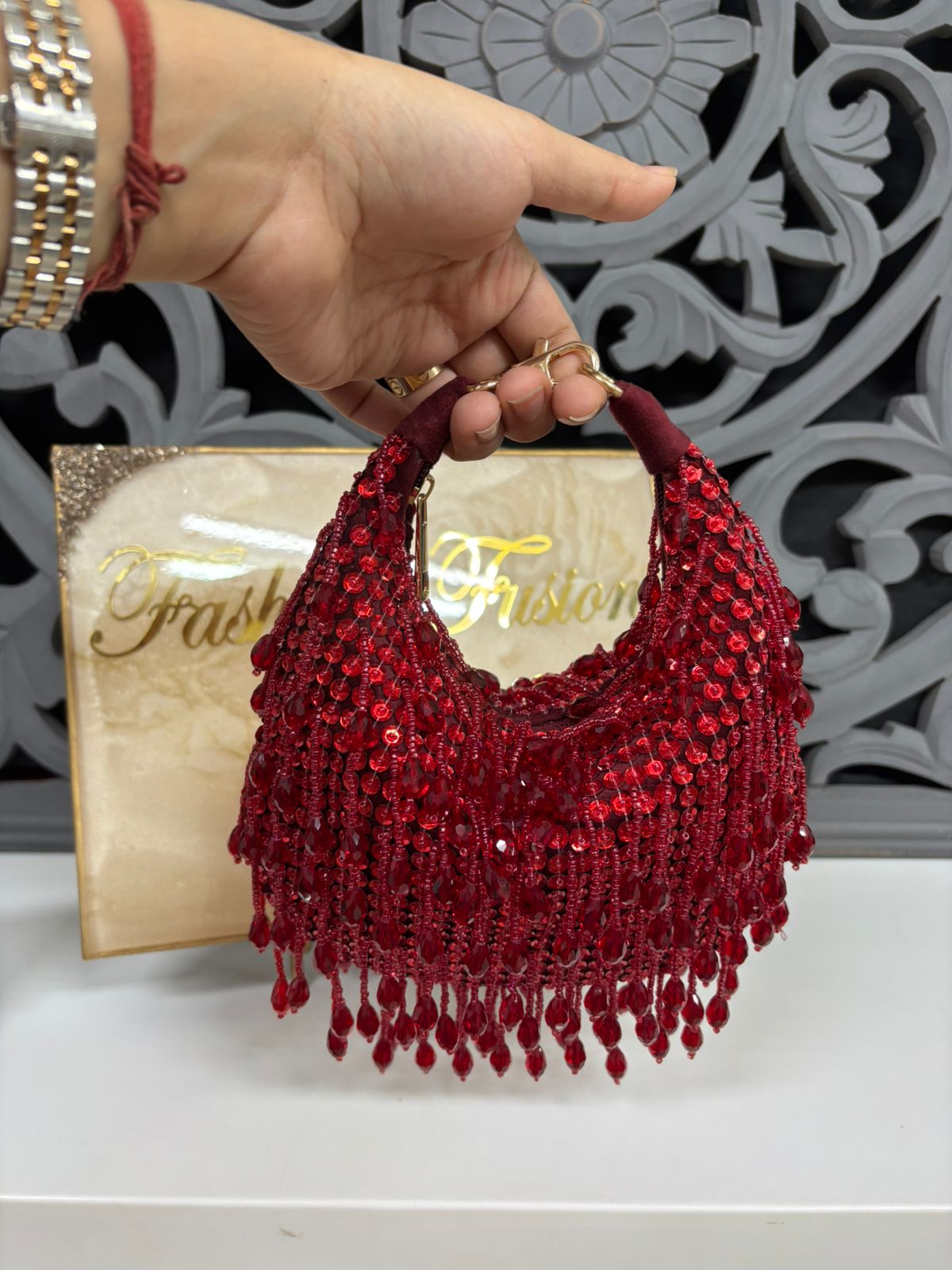 Red beaded handbag held by a hand with a decorative background