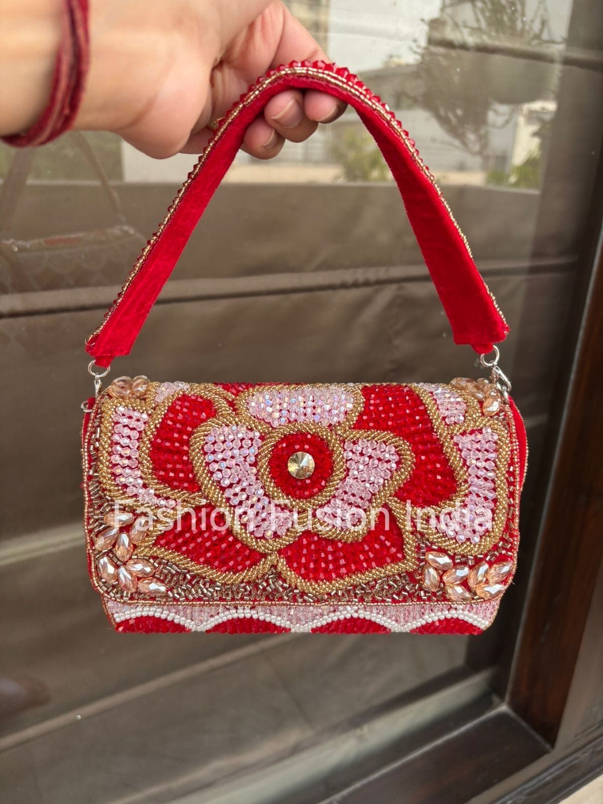 Decorative red handbag with intricate patterns held by a hand, with 'Fashion Fusion India' branding.