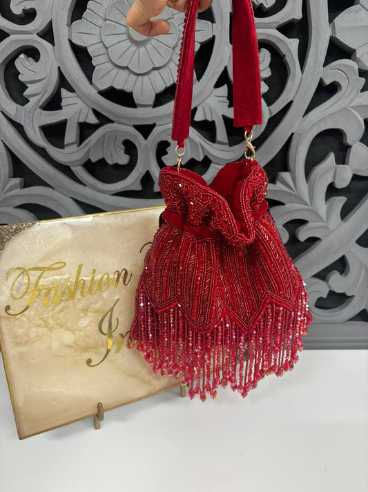 Red beaded handbag with decorative bow held against a decorative wall.