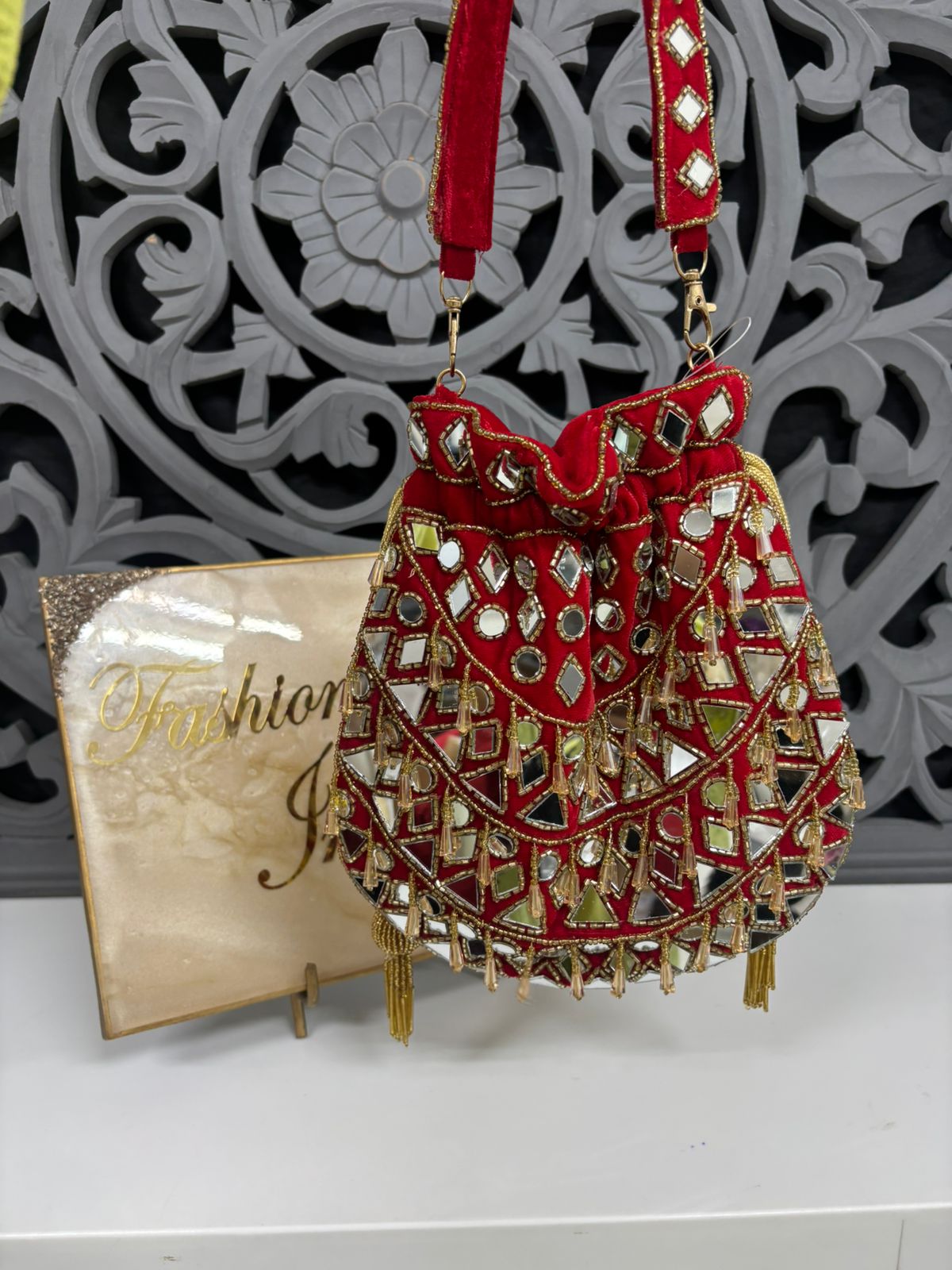 Decorative red handbag with gold accents on a white surface with a decorative gray background.