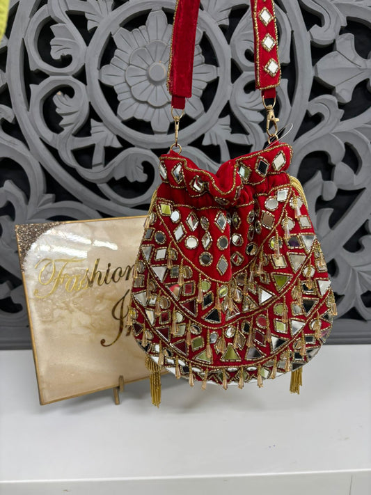 Decorative red handbag with gold accents on a white surface with a decorative gray background.