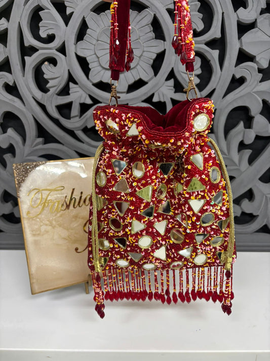Decorative red handbag with mirror work and beads on a white surface with a decorative wall in the background.