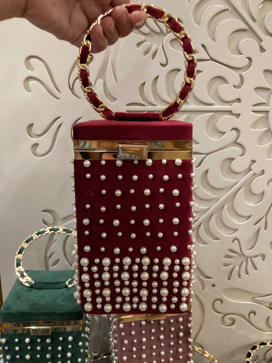Red handbag with pearl embellishments held by a hand against a decorative white background