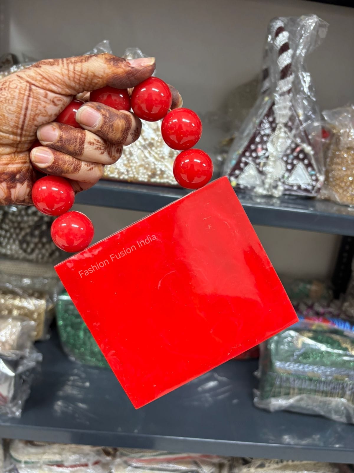 Hand holding a red beaded bracelet with a 'Fashion Fusion India' tag in the foreground.