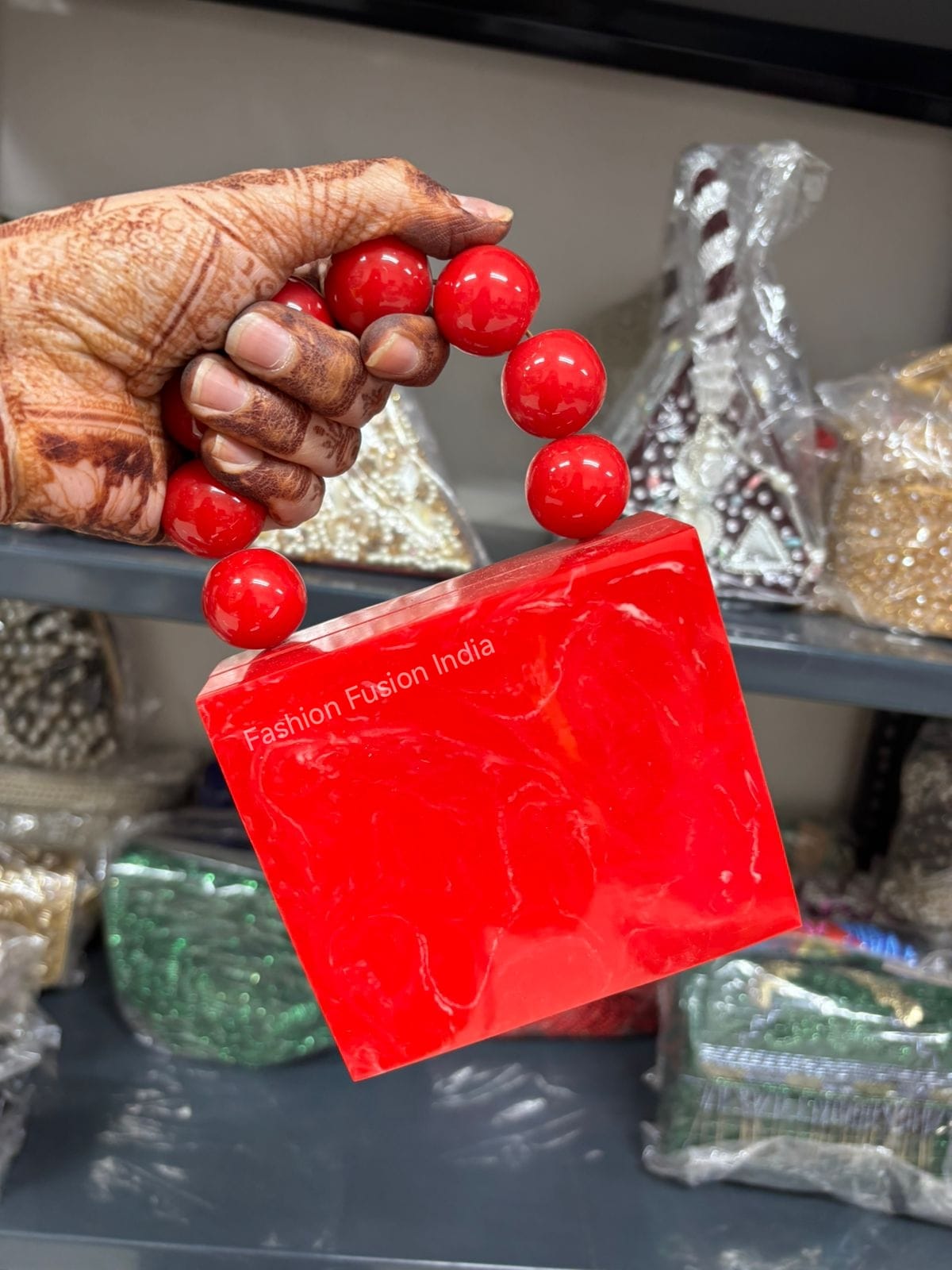 Hand holding red beads with a red card displaying 'Fashion Fusion India' in a blurred background.