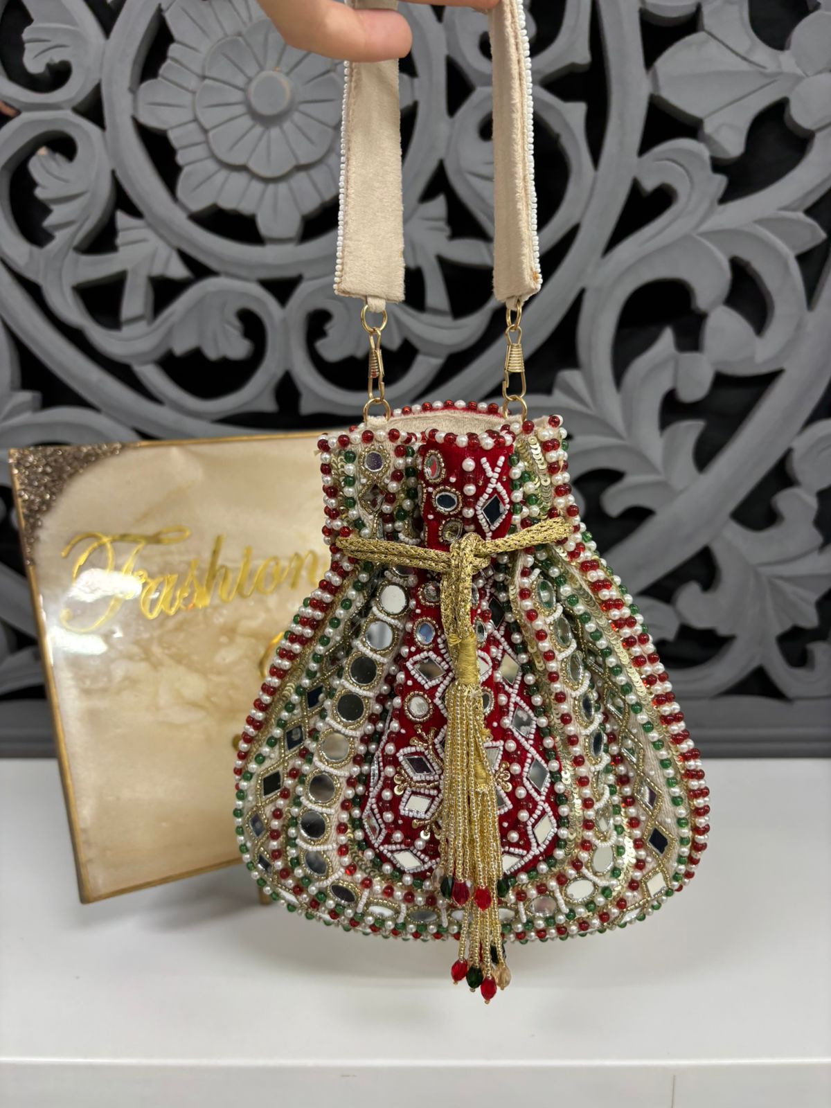 Decorative handbag with intricate designs and embellishments, held against a decorative wall.