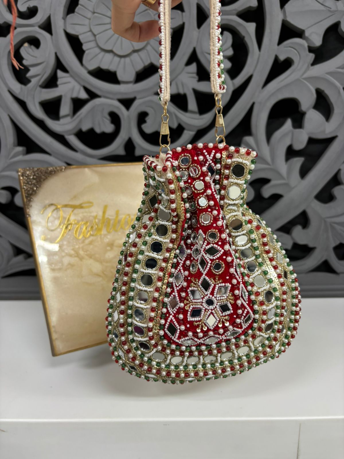 Decorative handbag with intricate patterns and beads on a white surface with a decorative background.