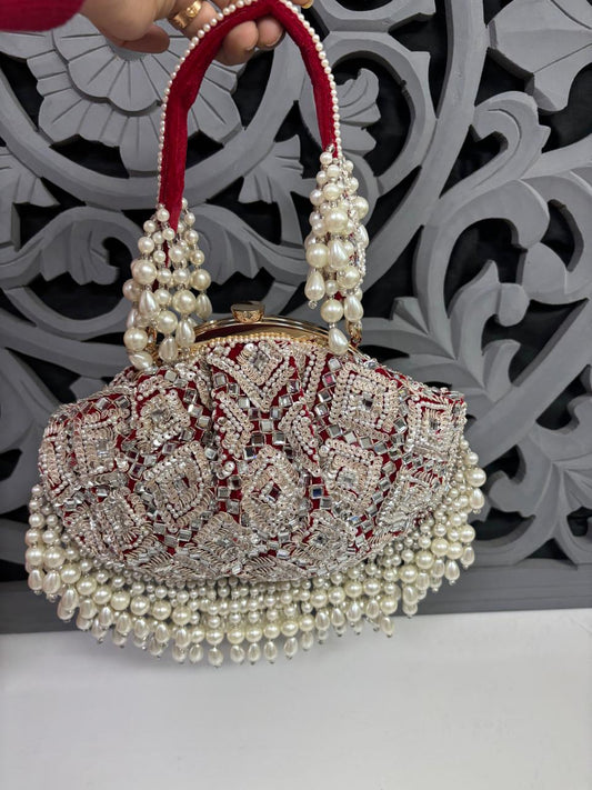 Decorative handbag with pearls and red accents held by a hand against an ornate wall.