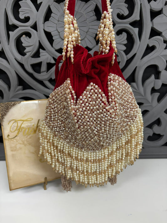 Decorative handbag with pearls and red velvet bow against a decorative wall.