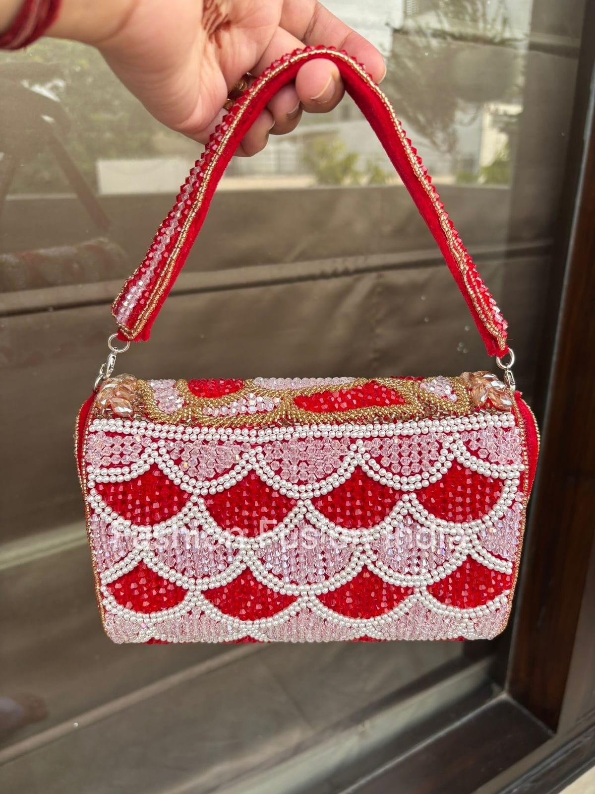 Red beaded handbag held by a hand with a blurred background