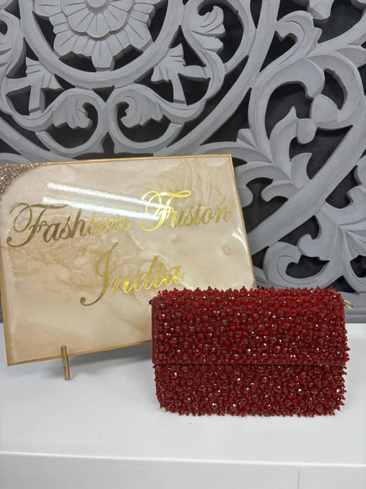 Red beaded clutch bag on a white surface with 'Fashion Fusion India' sign in the background.