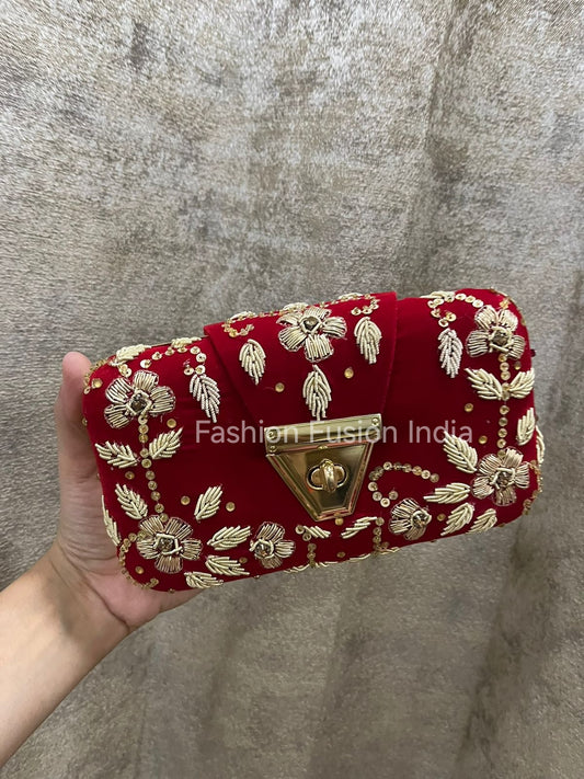 Red clutch bag with gold embroidery held by a hand against a gray background