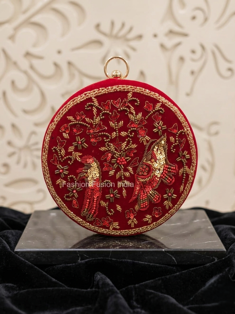 Red embroidered clutch bag with gold detailing on a black stand against a decorative white background