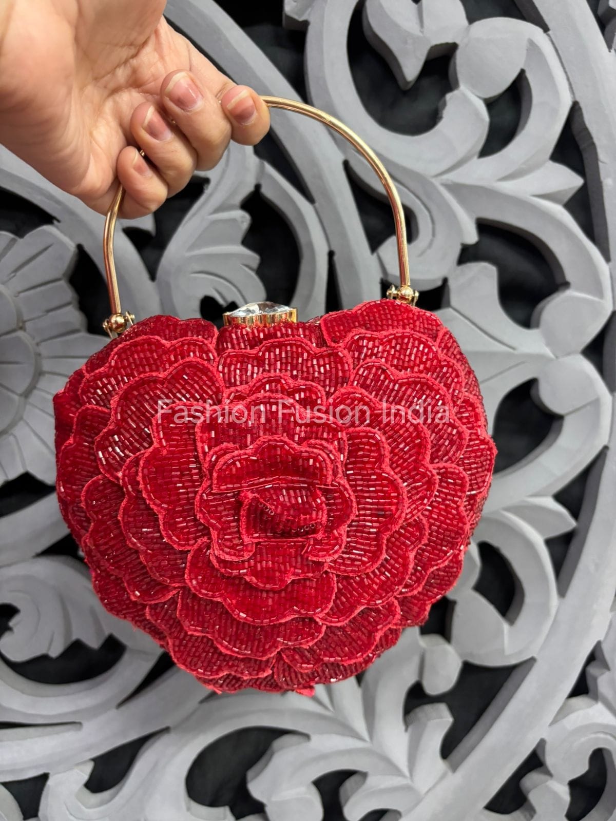 Red floral embroidered clutch held by a hand against an ornate white and black background.