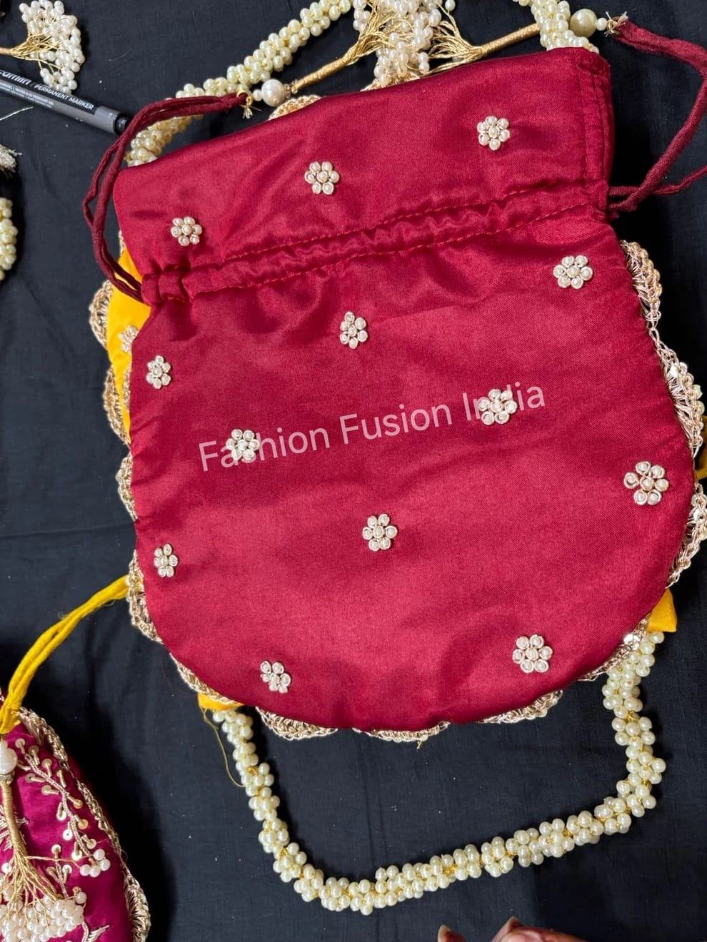 Red handbag with floral embroidery on a dark fabric background, featuring 'Fashion Fusion India' branding.