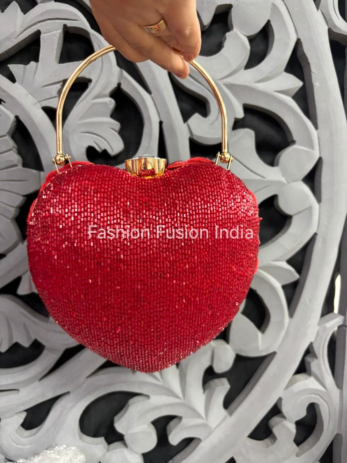 Red heart-shaped clutch bag with gold handle against a decorative white and black background.