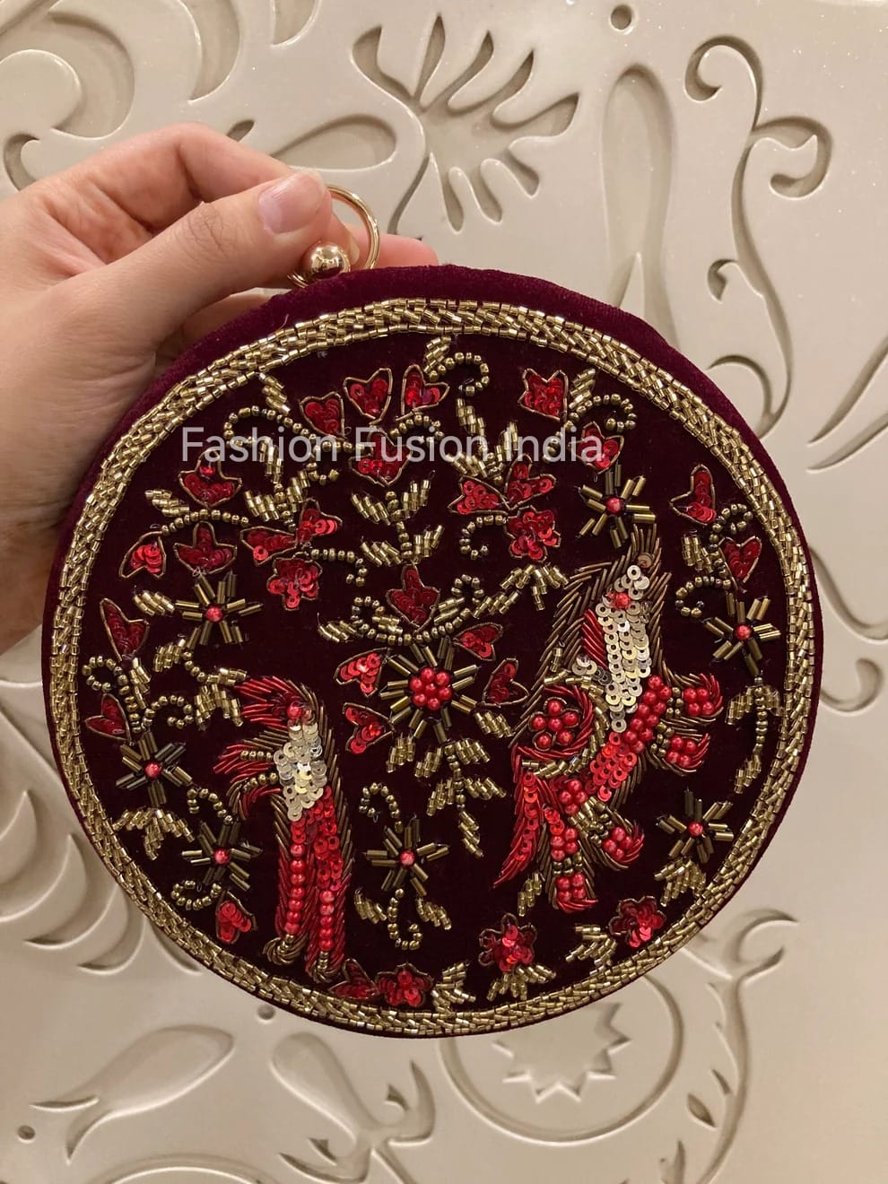 Round embroidered clutch held by a hand against a decorative white background
