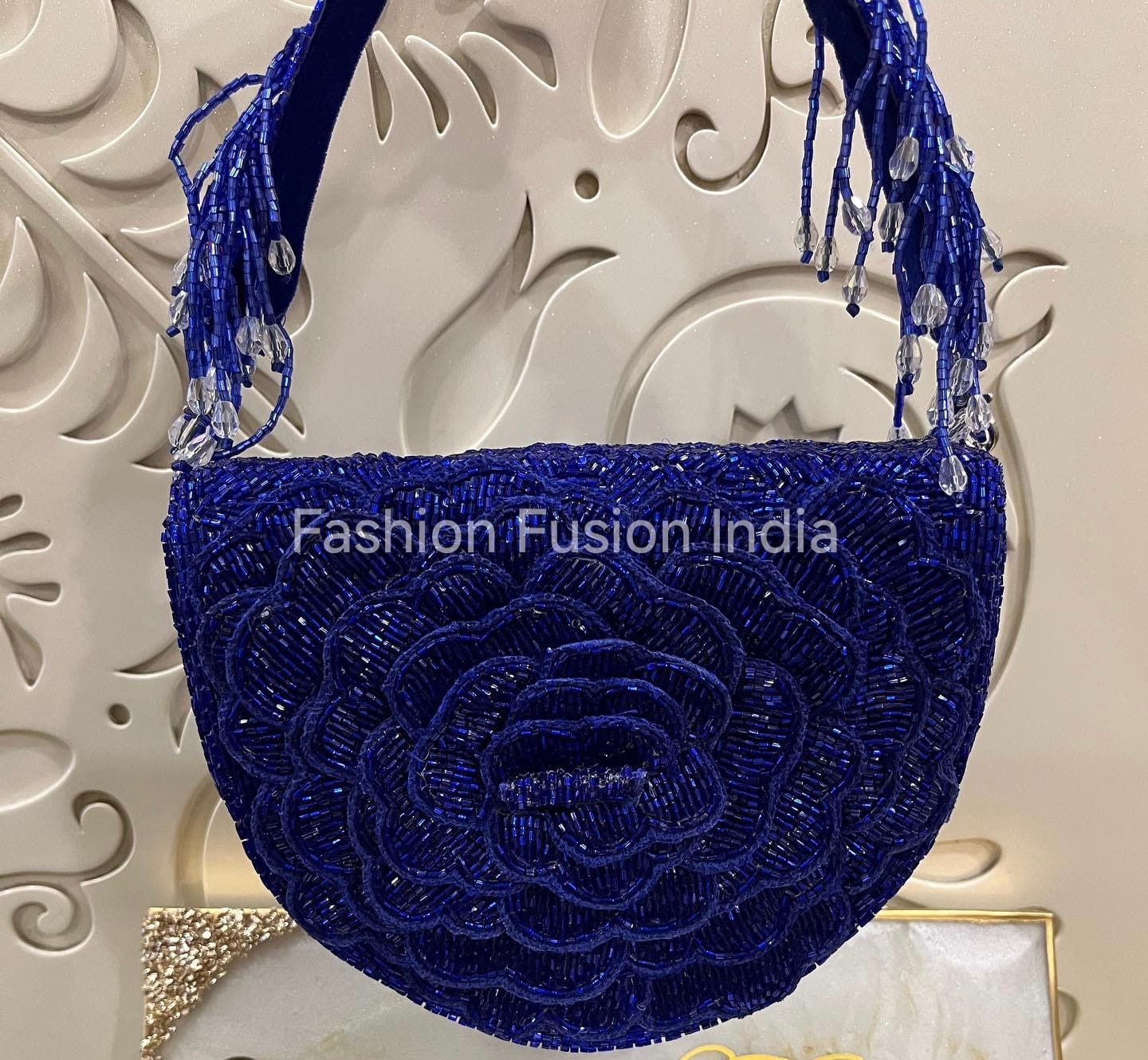 Blue beaded handbag with floral design against a decorative wall, branded 'Fashion Fusion India'.