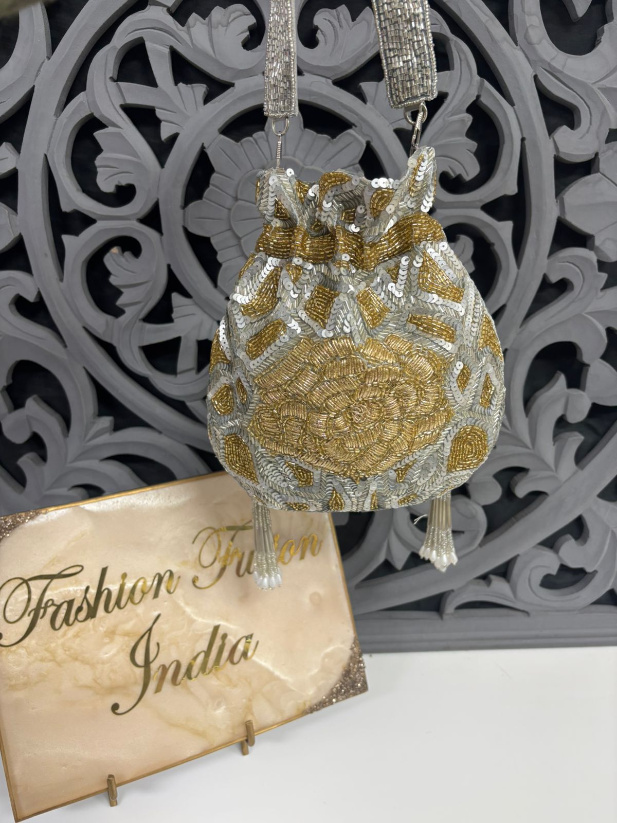Decorative gold and silver handbag with intricate patterns, displayed against a decorative gray background.