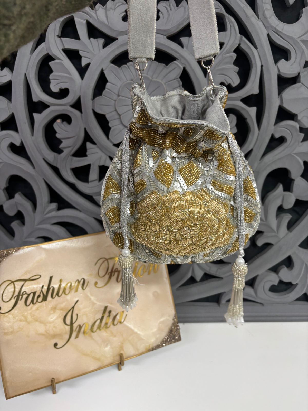 Decorative handbag with gold embroidery on a white surface with 'Fashion In India' sign.
