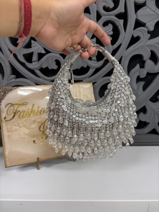 Silver beaded handbag held by a hand with a decorative background